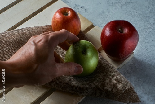 Closeup of a hand putting a green apple on a fabric on a board next to red apples photo