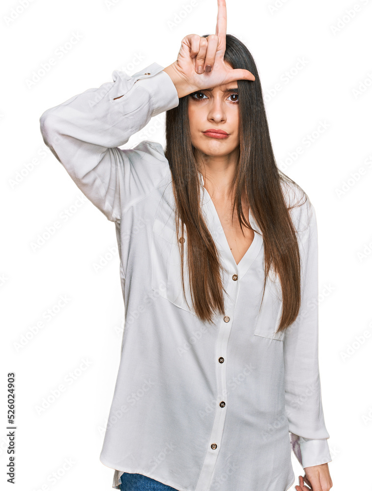 Young beautiful woman wearing casual white shirt making fun of people with fingers on forehead doing loser gesture mocking and insulting. Young beautiful woman wearing casual white shirt making fun of people with fingers on forehead doing loser gesture mocking and insulting.