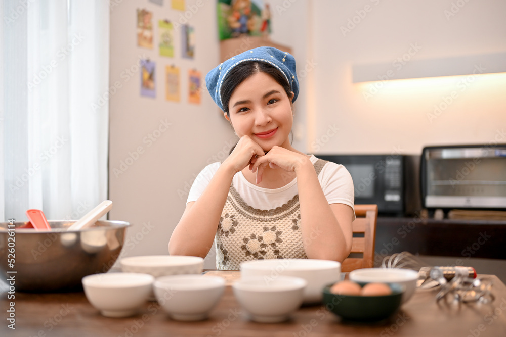 Attractive Asian female baker at the dining table with cupcake ingredients.