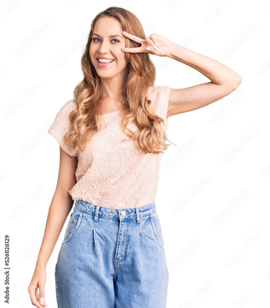 Young beautiful caucasian woman with blond hair wearing casual clothes doing peace symbol with fingers over face, smiling cheerful showing victory Young beautiful caucasian woman with blond hair wearing casual clothes doing peace symbol with fingers over face, smiling cheerful showing victory