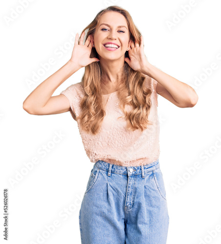 Young beautiful caucasian woman with blond hair wearing casual clothes trying to hear both hands on ear gesture, curious for gossip. hearing problem, deaf