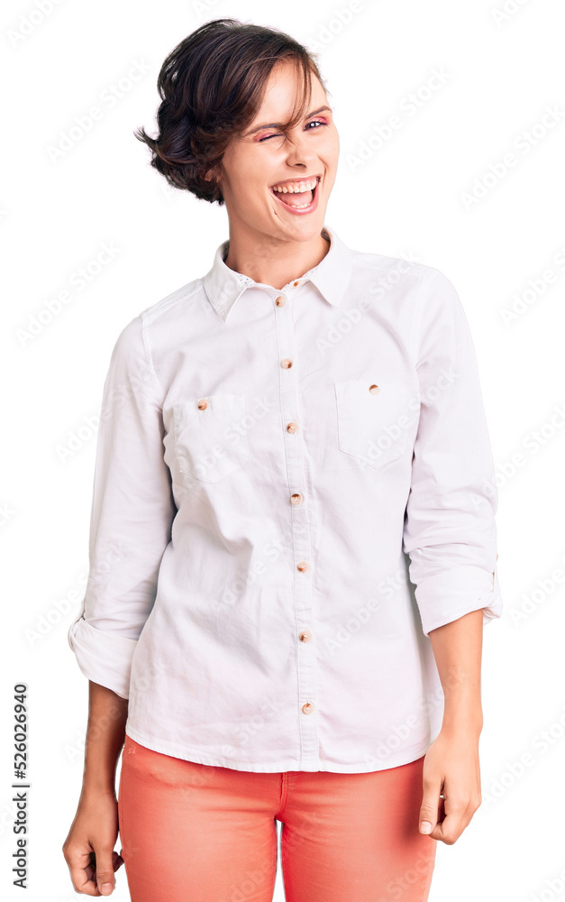 Beautiful young woman with short hair wearing elegant white shirt winking looking at the camera with sexy expression, cheerful and happy face. Beautiful young woman with short hair wearing elegant white shirt winking looking at the camera with sexy expression, cheerful and happy face.