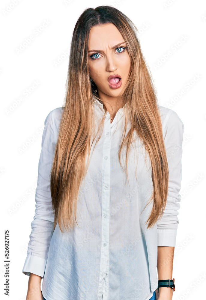 Beautiful caucasian woman wearing casual white shirt in shock face, looking skeptical and sarcastic, surprised with open mouth Beautiful caucasian woman wearing casual white shirt in shock face, looking skeptical and sarcastic, surprised with open mouth