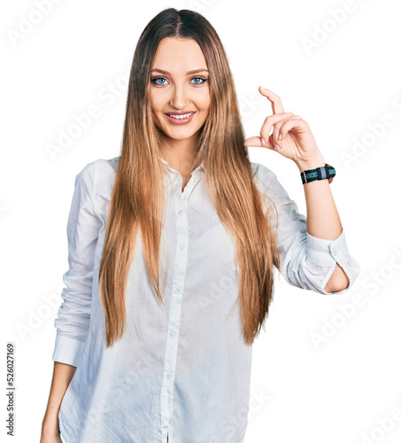 Beautiful caucasian woman wearing casual white shirt smiling and confident gesturing with hand doing small size sign with fingers looking and the camera. measure concept.