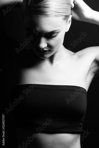 Fashion  beauty  style and make-up concept. Black and white studio portrait of beautiful and sexy woman with tight black clothes looking down and touching her hair with hands