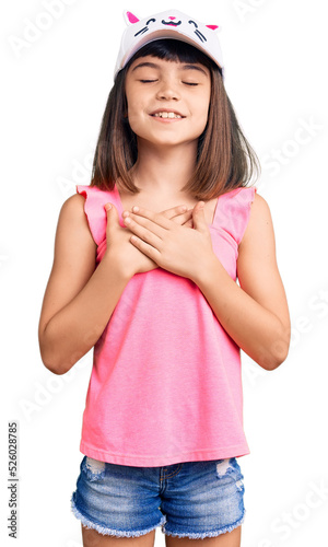 Young little girl with bang wearing funny kitty cap smiling with hands on chest with closed eyes and grateful gesture on face. health concept.