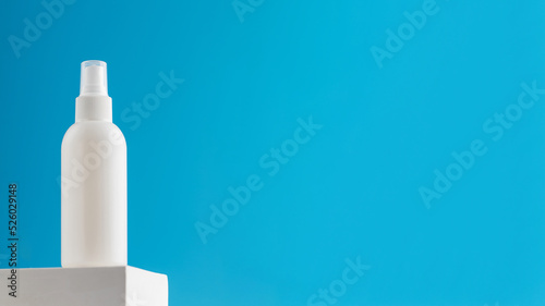 White spray mockup with air freshener or cosmetic product on a pedestal on a blue background.