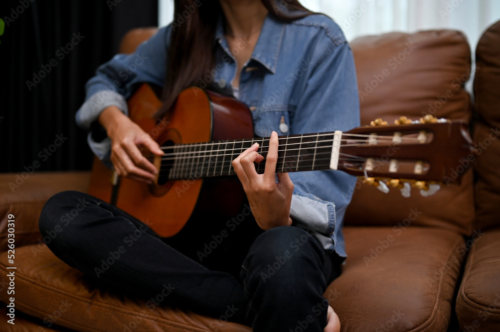 Female playing her classic guitar in the living room, on her leather sofa. cropped image