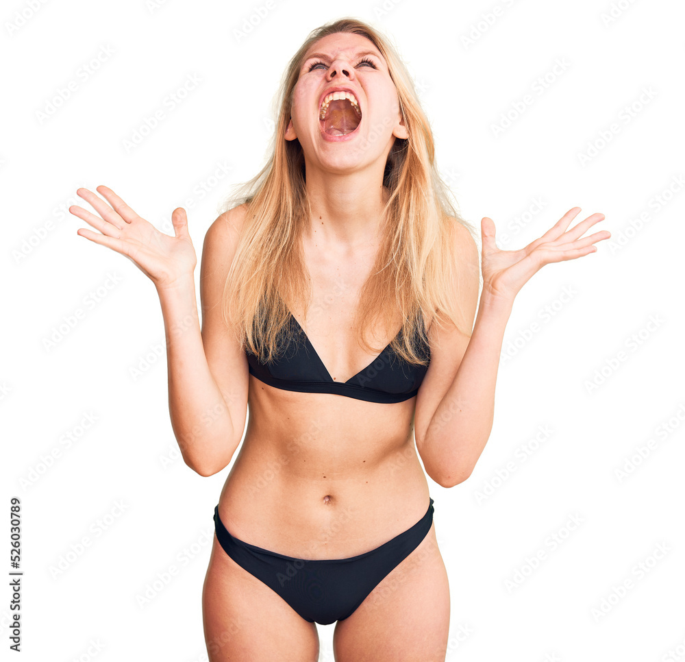 Young beautiful blonde woman wearing bikini crazy and mad shouting and yelling with aggressive expression and arms raised. frustration concept. Young beautiful blonde woman wearing bikini crazy and mad shouting and yelling with aggressive expression and arms raised. frustration concept.