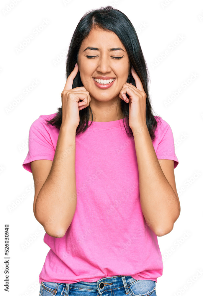 Beautiful asian young woman wearing casual pink t shirt covering ears with fingers with annoyed expression for the noise of loud music. deaf concept. Beautiful asian young woman wearing casual pink t shirt covering ears with fingers with annoyed expression for the noise of loud music. deaf concept.