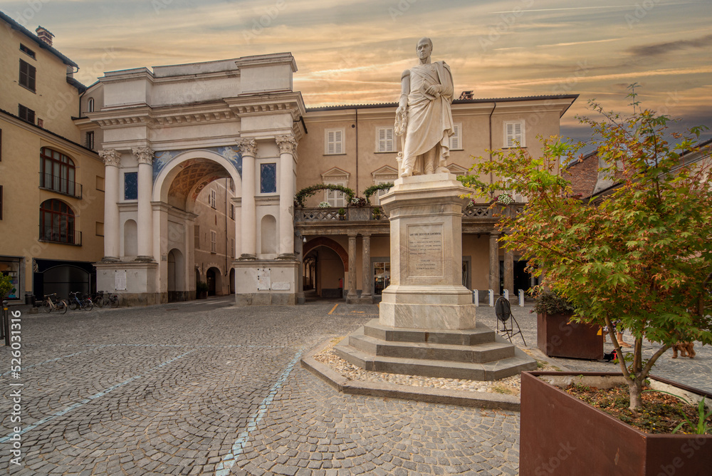 Savigliano, Piedmont Italy - August 10, 2022: triumphal arch or Monumental to Vittorio Emanuele Primo (XVI century) and the statue of Santore Derossi of Santarosa in Santarosa Square. Sunset time