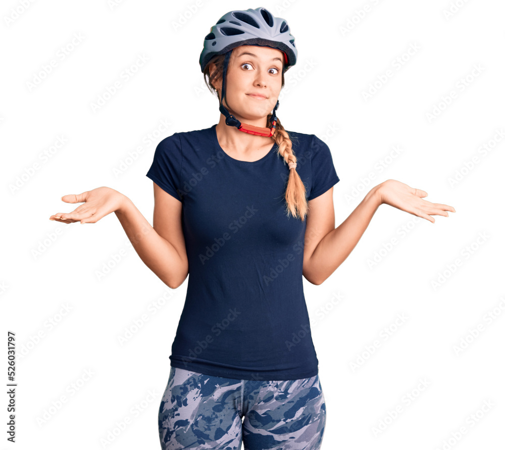 Beautiful caucasian woman wearing bike helmet clueless and confused expression with arms and hands raised. doubt concept. Beautiful caucasian woman wearing bike helmet clueless and confused expression with arms and hands raised. doubt concept.