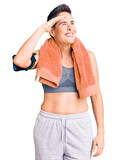 Young woman with short hair wearing sportswear and towel using smartphone very happy and smiling looking far away with hand over head. searching concept.