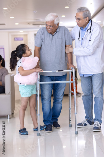 Granddaughter with male doctor teaching disabled grandfather to use walker at hospital 