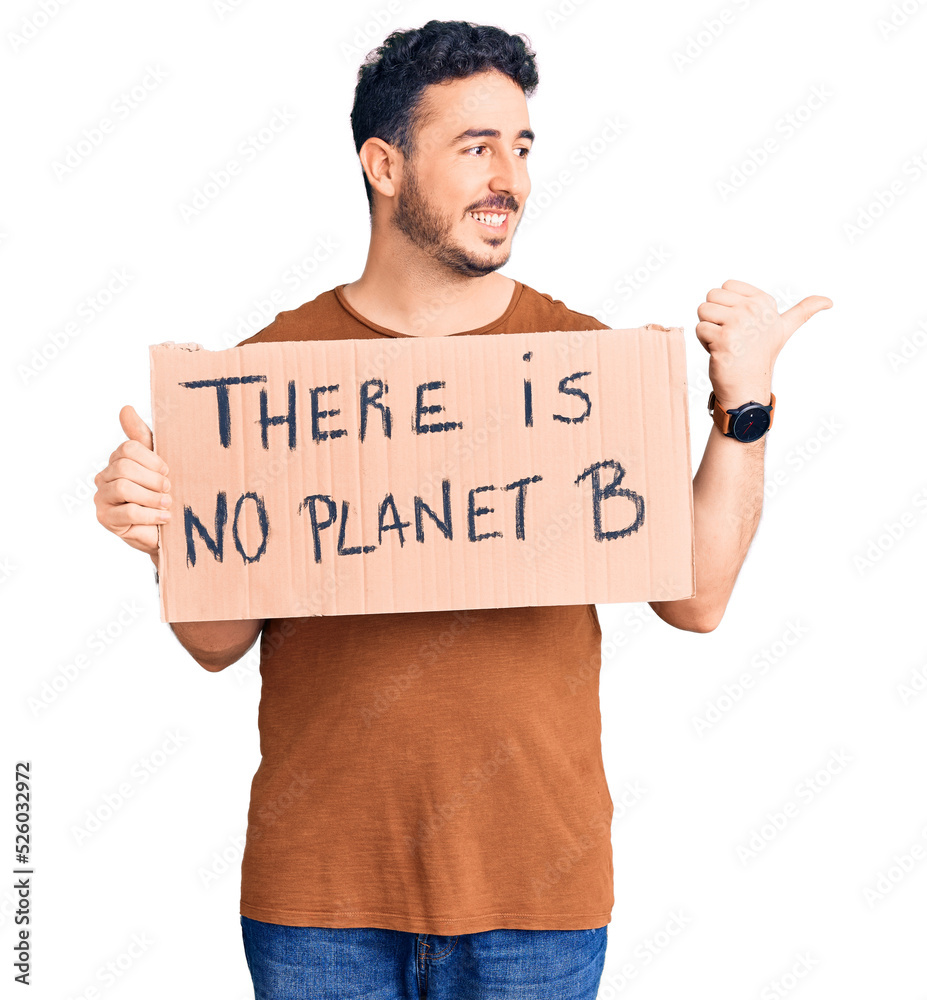 Young hispanic man holding there is no planet b banner pointing thumb up to the side smiling happy with open mouth