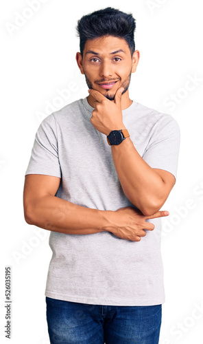 Handsome latin american young man wearing casual tshirt looking confident at the camera smiling with crossed arms and hand raised on chin. thinking positive.