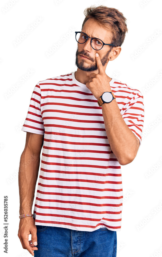 Handsome blond man with beard wearing casual clothes and glasses pointing to the eye watching you gesture, suspicious expression Handsome blond man with beard wearing casual clothes and glasses pointing to the eye watching you gesture, suspicious expression