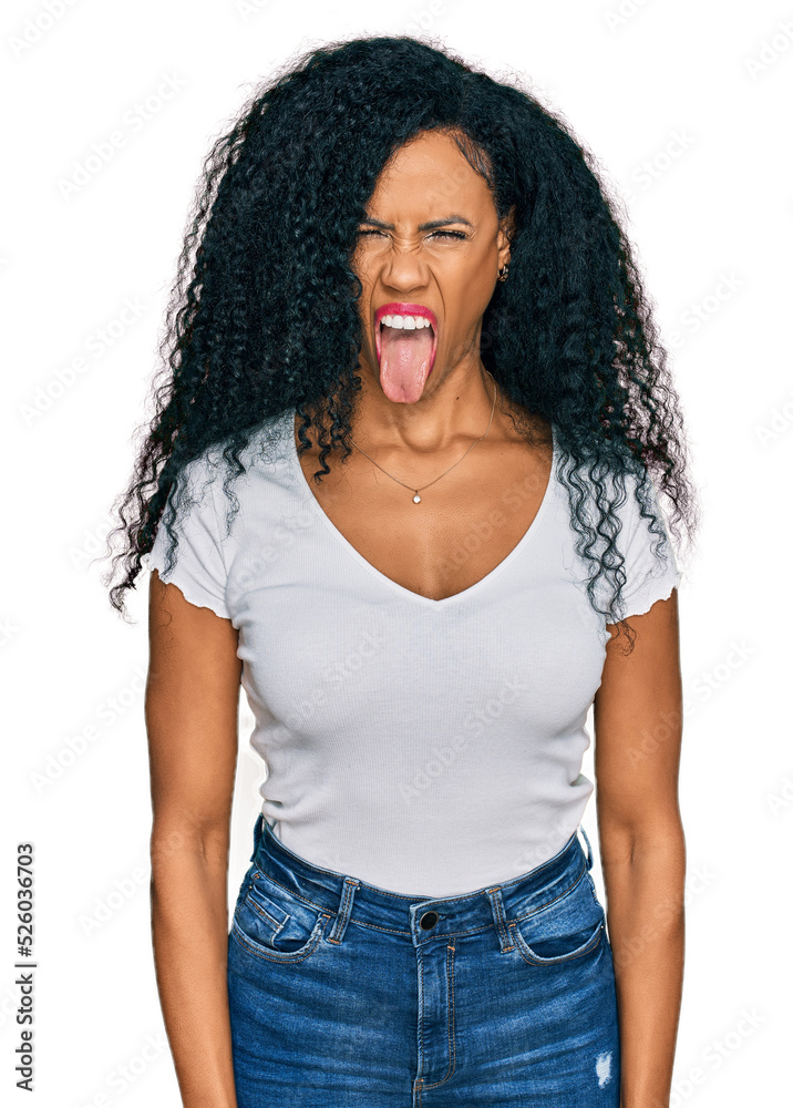 Middle age african american woman wearing casual white t shirt sticking tongue out happy with funny expression. emotion concept. Middle age african american woman wearing casual white t shirt sticking tongue out happy with funny expression. emotion concept.