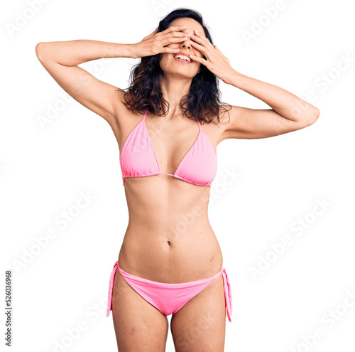 Young beautiful hispanic woman wearing bikini covering eyes with hands smiling cheerful and funny. blind concept.