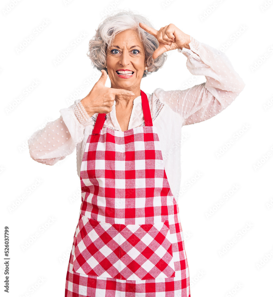 Senior grey-haired woman wearing apron smiling making frame with hands and fingers with happy face. creativity and photography concept. Senior grey-haired woman wearing apron smiling making frame with hands and fingers with happy face. creativity and photography concept.