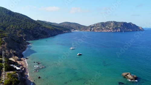 2 boats in front of cliff beach in turquoise water.
Buttery soft aerial view flight pedestal down drone footage of Aigües Blanques Ibiza summer day july 2022. P. Marnitz 4k Cinematic view from above photo