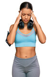 Beautiful hispanic woman wearing sportswear and headphones suffering from headache desperate and stressed because pain and migraine. hands on head.