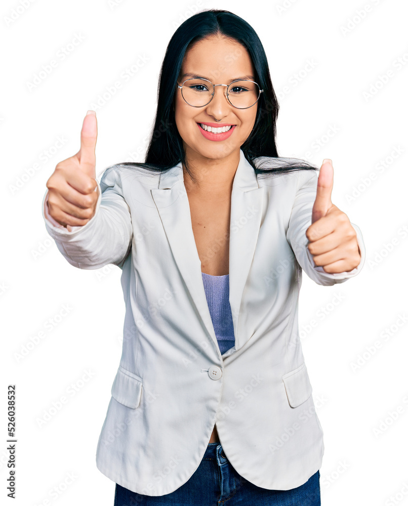 Beautiful hispanic woman with nose piercing wearing business jacket and glasses approving doing positive gesture with hand, thumbs up smiling and happy for success. winner gesture.