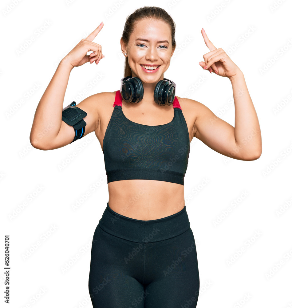 Beautiful blonde woman wearing gym clothes and using headphones smiling pointing to head with both hands finger, great idea or thought, good memory Beautiful blonde woman wearing gym clothes and using headphones smiling pointing to head with both hands finger, great idea or thought, good memory