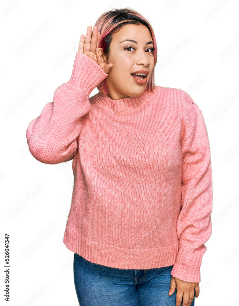 Hispanic woman with pink hair wearing casual winter sweater smiling with hand over ear listening an hearing to rumor or gossip. deafness concept. Hispanic woman with pink hair wearing casual winter sweater smiling with hand over ear listening an hearing to rumor or gossip. deafness concept.