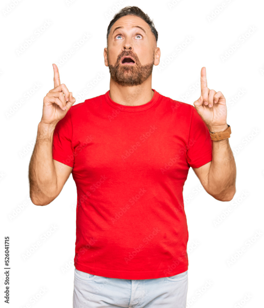 Handsome middle age man wearing casual red tshirt amazed and surprised looking up and pointing with fingers and raised arms. Handsome middle age man wearing casual red tshirt amazed and surprised looking up and pointing with fingers and raised arms.