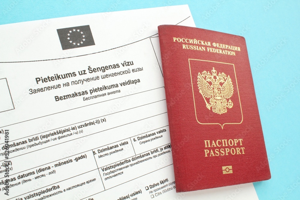 Schengen visa application form in Russian and Latvian language and passport on blue background. Prohibition and suspension of visas for Russian tourists to travel to Europe Union and Baltic States Schengen visa application form in Russian and Latvian language and passport on blue background. Prohibition and suspension of visas for Russian tourists to travel to Europe Union and Baltic States