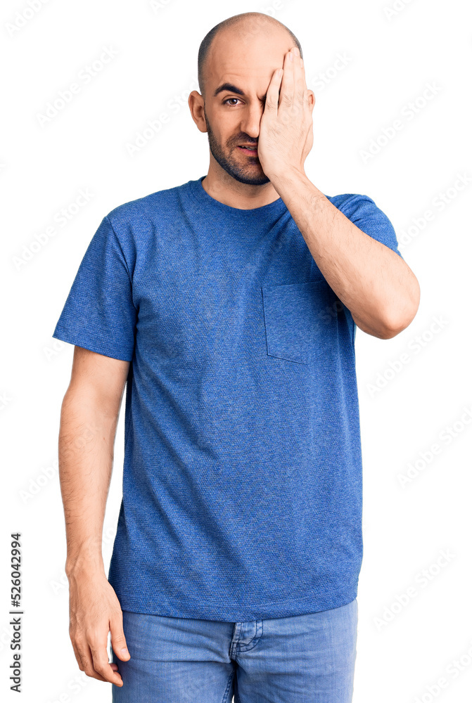 Young handsome man wearing casual t shirt covering one eye with hand, confident smile on face and surprise emotion. Young handsome man wearing casual t shirt covering one eye with hand, confident smile on face and surprise emotion.
