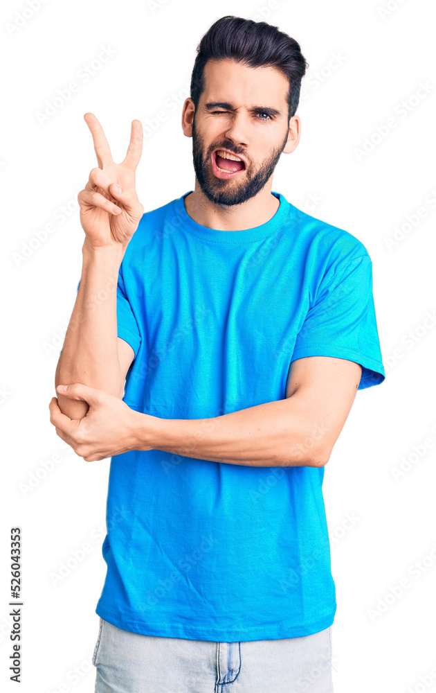 Young handsome man with beard wearing casual t-shirt smiling with happy face winking at the camera doing victory sign with fingers. number two. Young handsome man with beard wearing casual t-shirt smiling with happy face winking at the camera doing victory sign with fingers. number two.