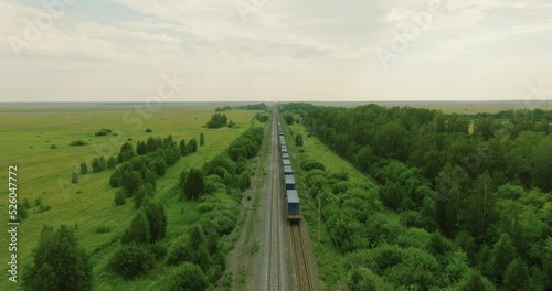 Freight long train carries with cargo carriages in flat swampland landscape through a difficult part of  Siberian railways. Aerial drone view at summer sunset