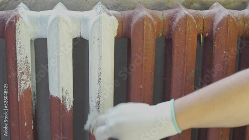 A worker hand paints a cast-iron radiator white dye