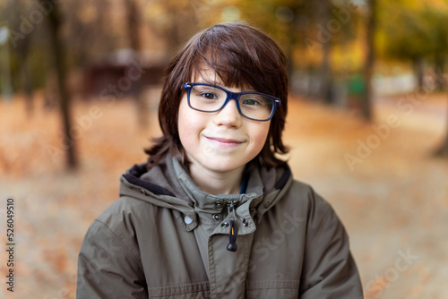 Close up portrait of a young myopic teenager boy with glasses, smiling child outdoor in autumn in the park.