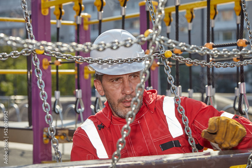 A specialist repairs the playground. A specialist in a white construction helmet and a red jumpsuit.	