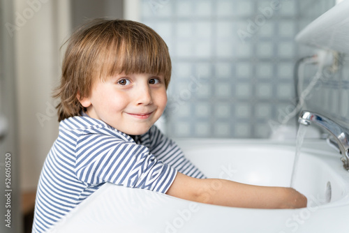 Toddler boy wearing striped t-shirt washing his hands in the bathroom. Child hygiene concept.