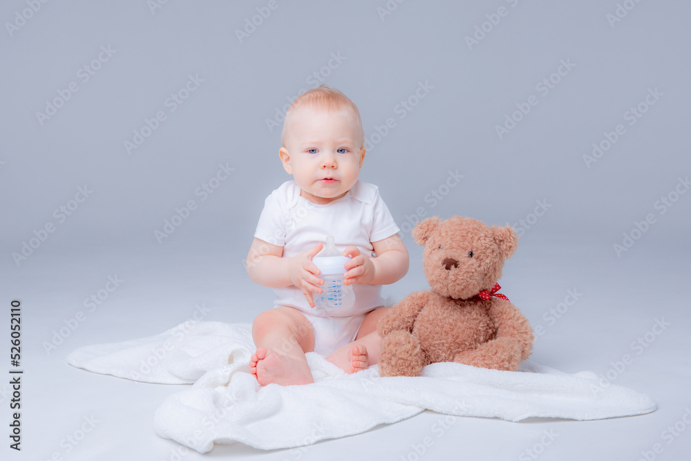 a baby boy in a white bodysuit sits with a teddy bear on a white background, holding a bottle of water , drinking water a baby boy in a white bodysuit sits with a teddy bear on a white background, holding a bottle of water , drinking water