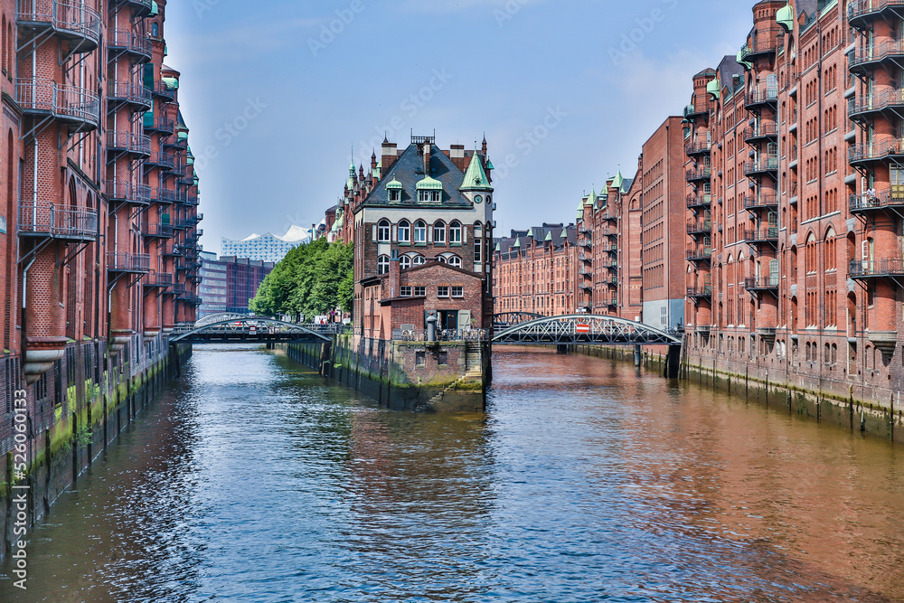 Foto von Hamburg Altstadt. Rote alte Reihenhäuser, verbunden durch Brücken. Sie liegen auf ruhigem Wasser, Kanäle. Darüber der klare wolkenlose Himmel. Bäume hinter den Häusern. Europäische Stadt.