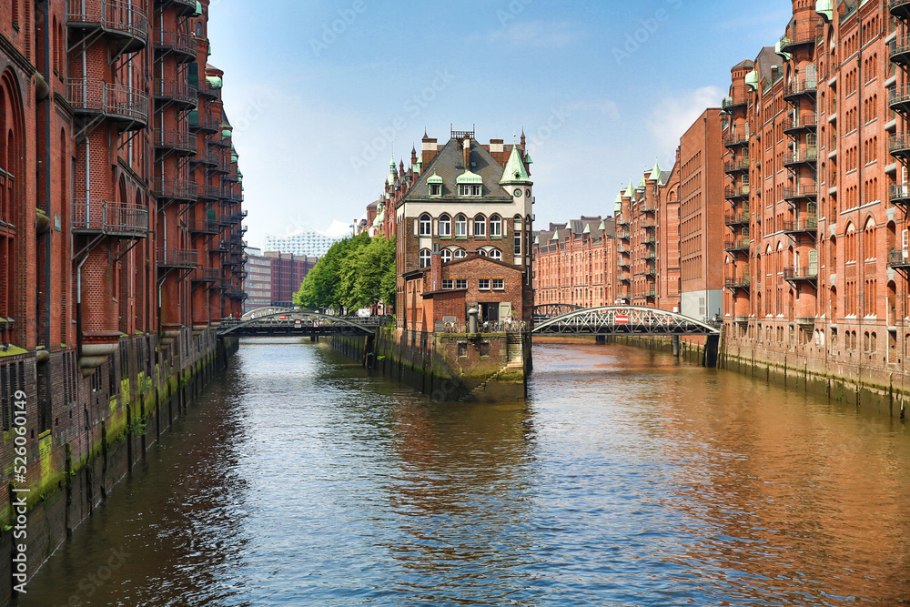 Foto von Hamburg Altstadt. Rote alte Reihenhäuser, verbunden durch Brücken. Sie liegen auf ruhigem Wasser, Kanäle. Darüber der klare wolkenlose Himmel. Bäume hinter den Häusern. Europäische Stadt.