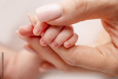 Close-up of a baby s small hand with tiny fingers and arm of mother on a white background. Newborn baby holding the finger of parents after birth The bond between mother and child Happy family concept