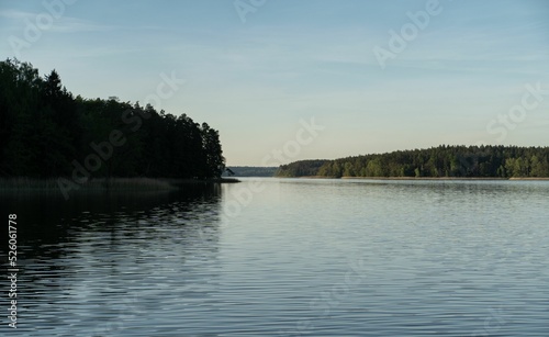 Clear sky and tall trees reflected on the still water of the Jeziorak lake photo