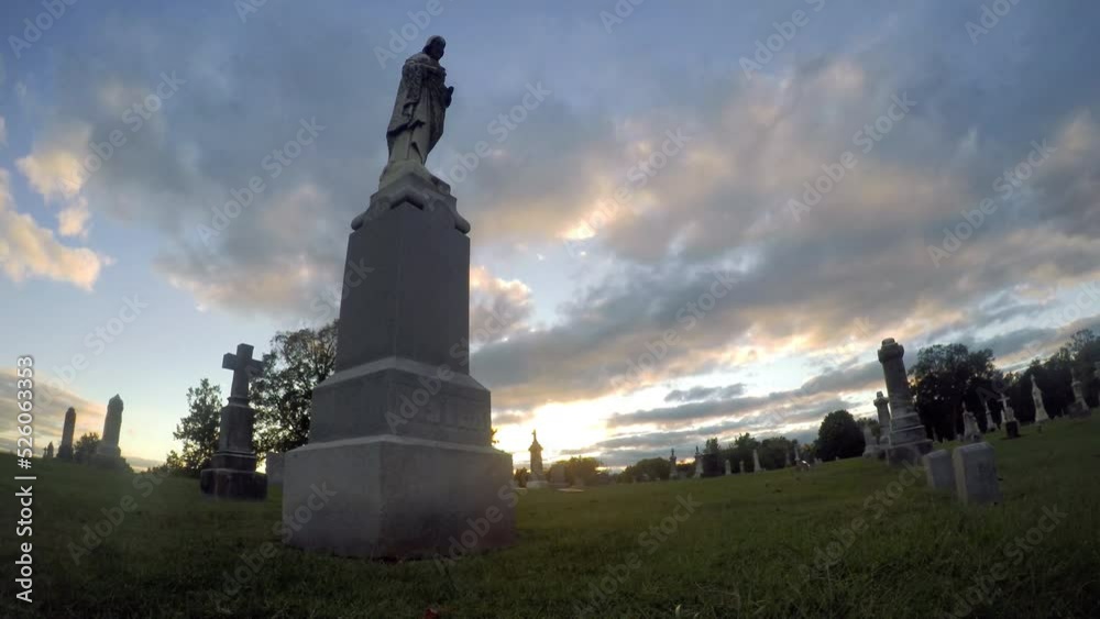A time lapse shot of the setting sun and moving clouds over a tombstone at a cemetary A time lapse shot of the setting sun and moving clouds over a tombstone at a cemetary