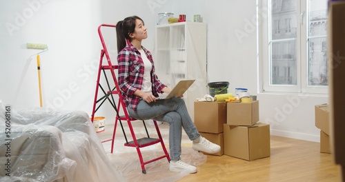 Billede på lærred Joyful Asian young beautiful female interior designer sitting on red ladder in e