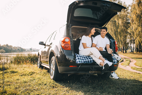 Happy traveler couple sitting in car open trunk and watch sunrise © stenkovlad