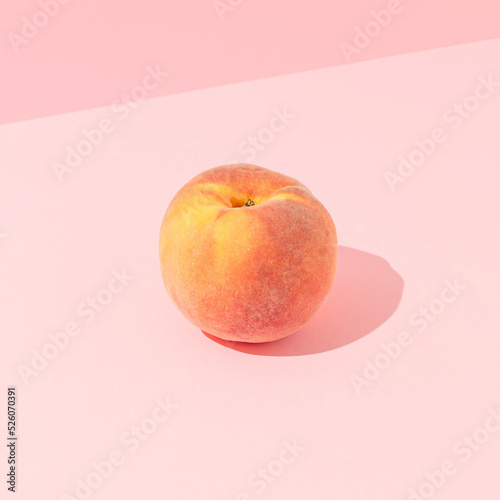 Single ripe peach fruit with sunny day shadow against pastel pink background. Minimal healthy snack food composition.