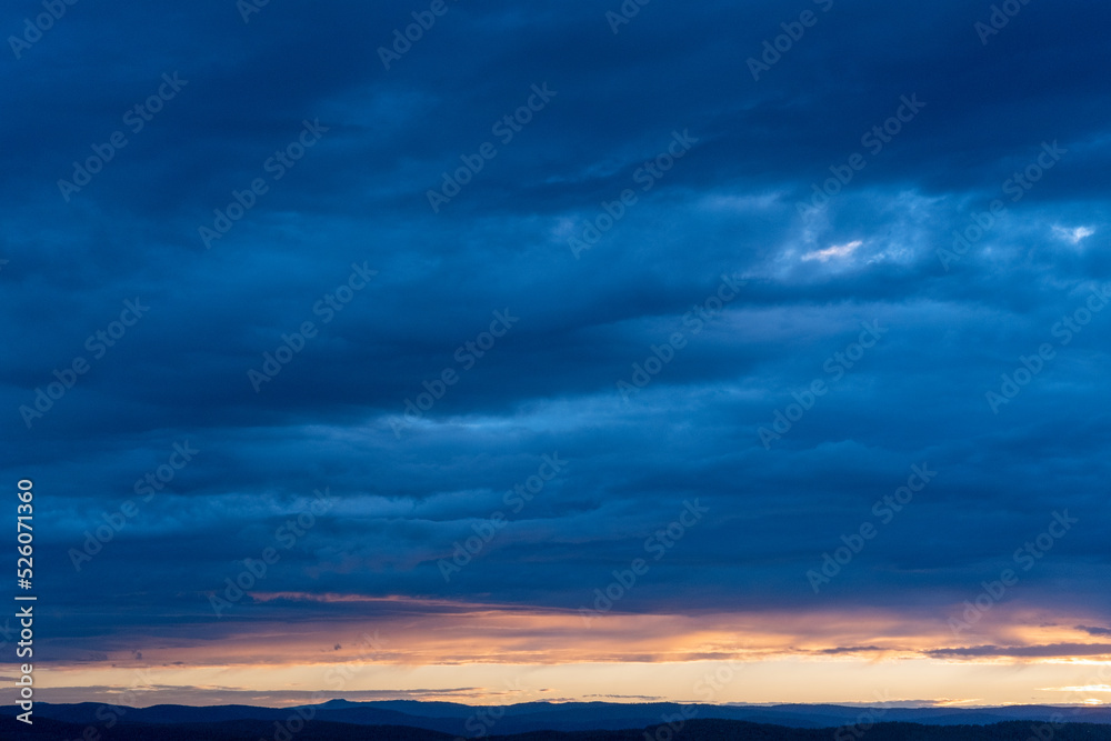 Evening sky with illuminated clouds, amazing sunset and majestic sunlight breaking through the clouds and leaving streaks of rays on the background of a dusky dark blue sky