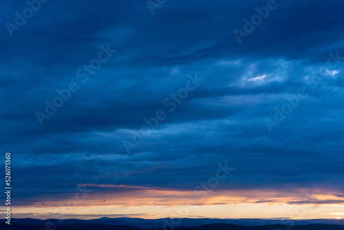 Evening sky with illuminated clouds, amazing sunset and majestic sunlight breaking through the clouds and leaving streaks of rays on the background of a dusky dark blue sky