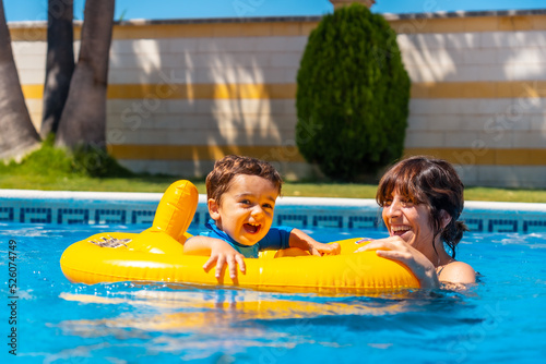 Smiling mother playing with her son with a yellow float in the pool © unai